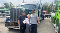 Three professionals posing together in front of blue and green commercial trucks at a trucking industry event