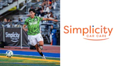 Soccer player in green patterned jersey controls ball during match with Simplicity Car Care sponsorship signage visible