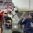 Volunteers restoring a vintage car at an indoor workshop event, with team members working on vehicle body panels and doors.