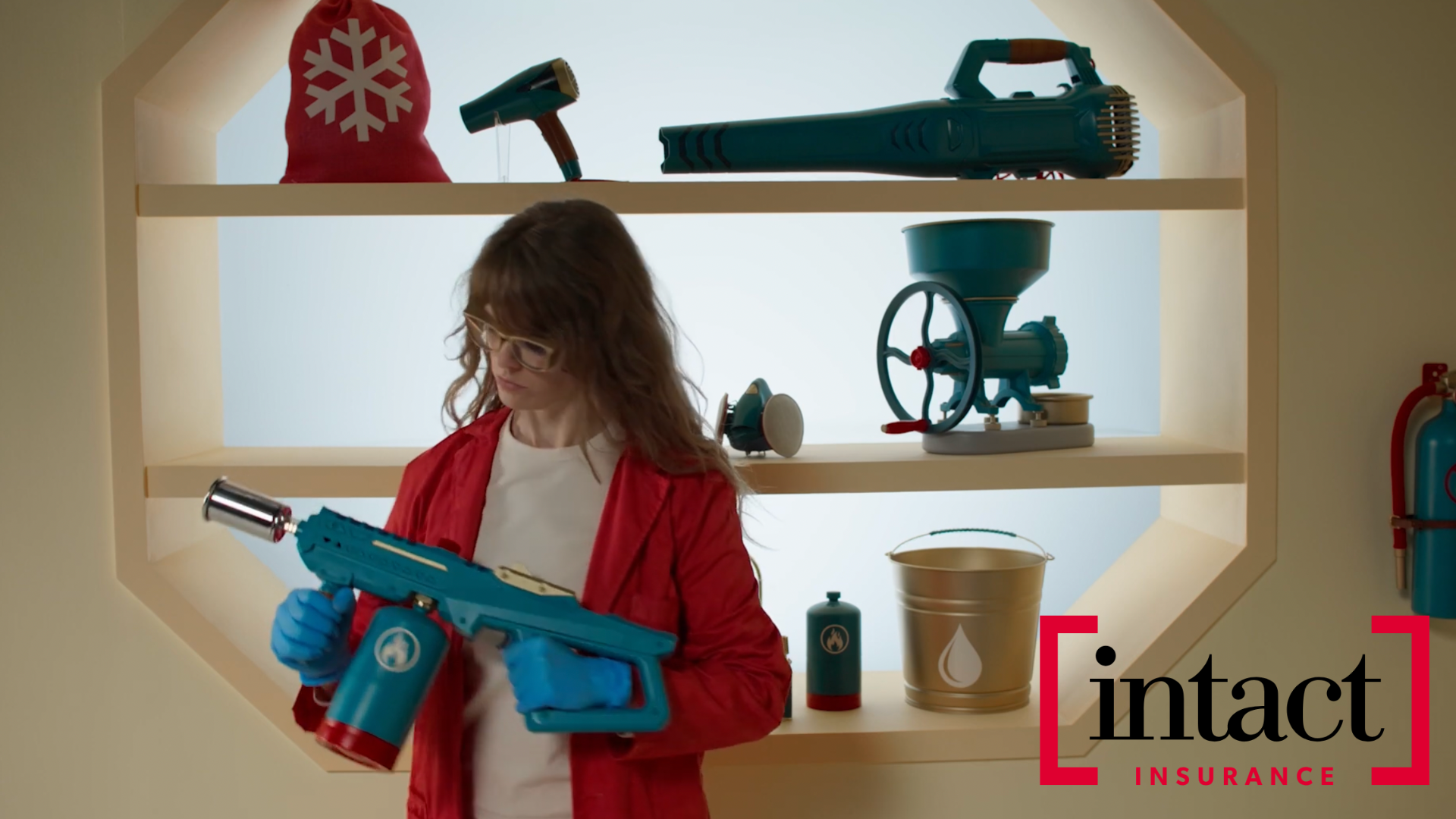 Woman in red cardigan examining blue power tool with workshop equipment and Intact Insurance logo