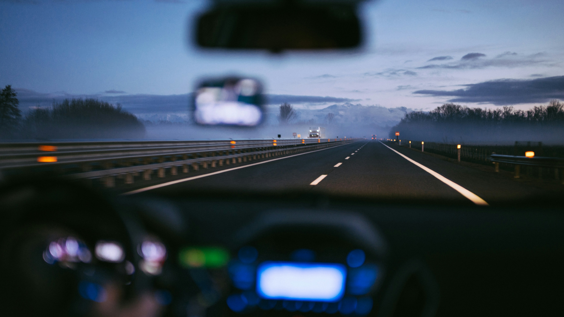 Highway view from car dashboard at dusk with oncoming traffic and guardrails under twilight sky