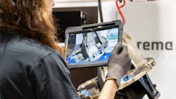Technician holding rugged tablet displaying industrial equipment footage on job site