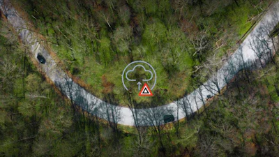 Aerial view of winding forest road with cloud and warning triangle icons overlay
