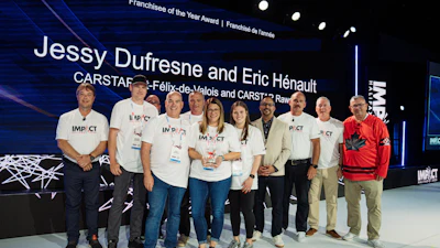 Group of award recipients and team members standing together at Franchisee of the Year Award ceremony with blue stage backdrop