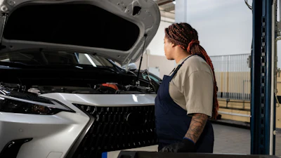 Female mechanic in work uniform inspecting open engine of white vehicle in professional garage setting