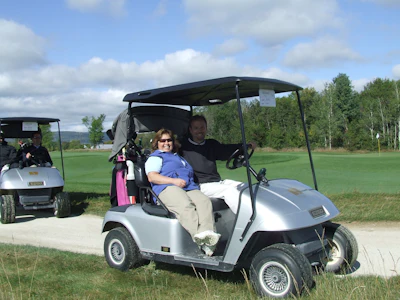 Man and child riding in a white golf cart on a scenic golf course with green fairways and trees
