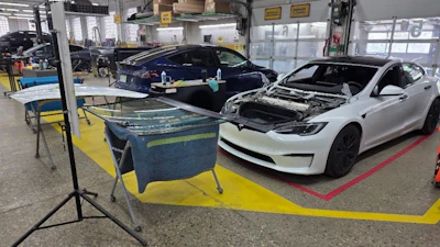 Automotive service facility with white Tesla and dark sedan undergoing maintenance in industrial workshop.