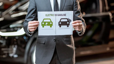 Businessman holding electric vs gasoline vehicle comparison chart in automotive workshop