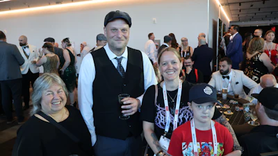Four people smiling at a formal event with other attendees and tables visible in the background