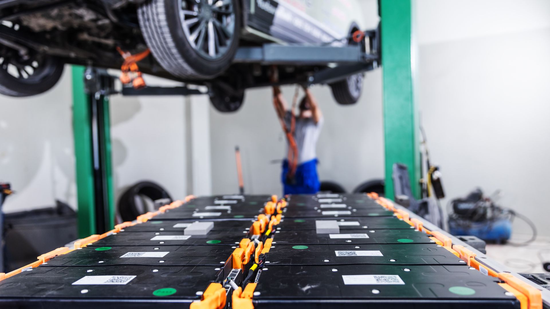 Automotive technician working under vehicle lifted on green hydraulic lift in professional service garage