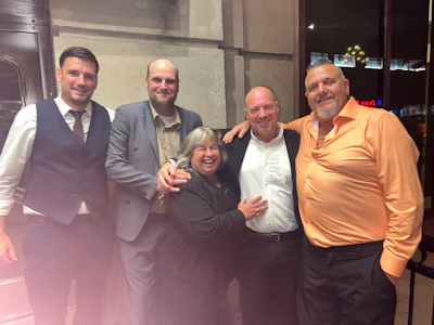 Five people smiling together at an indoor event, dressed in business casual attire