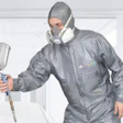 Professional painter wearing gray protective suit, hood, and respirator mask while holding spray gun equipment