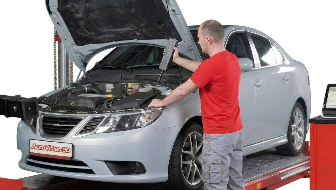 Mechanic in red shirt inspecting white sedan engine on diagnostic lift with AcuVision equipment