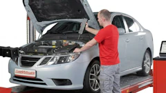 Mechanic in red shirt inspecting white sedan engine on diagnostic lift with AcuVision equipment