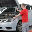 Mechanic in red shirt inspecting white sedan engine on diagnostic lift with AcuVision equipment