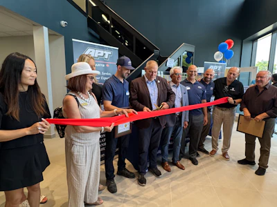 Group of professionals and community members participating in ribbon-cutting ceremony at APT facility opening