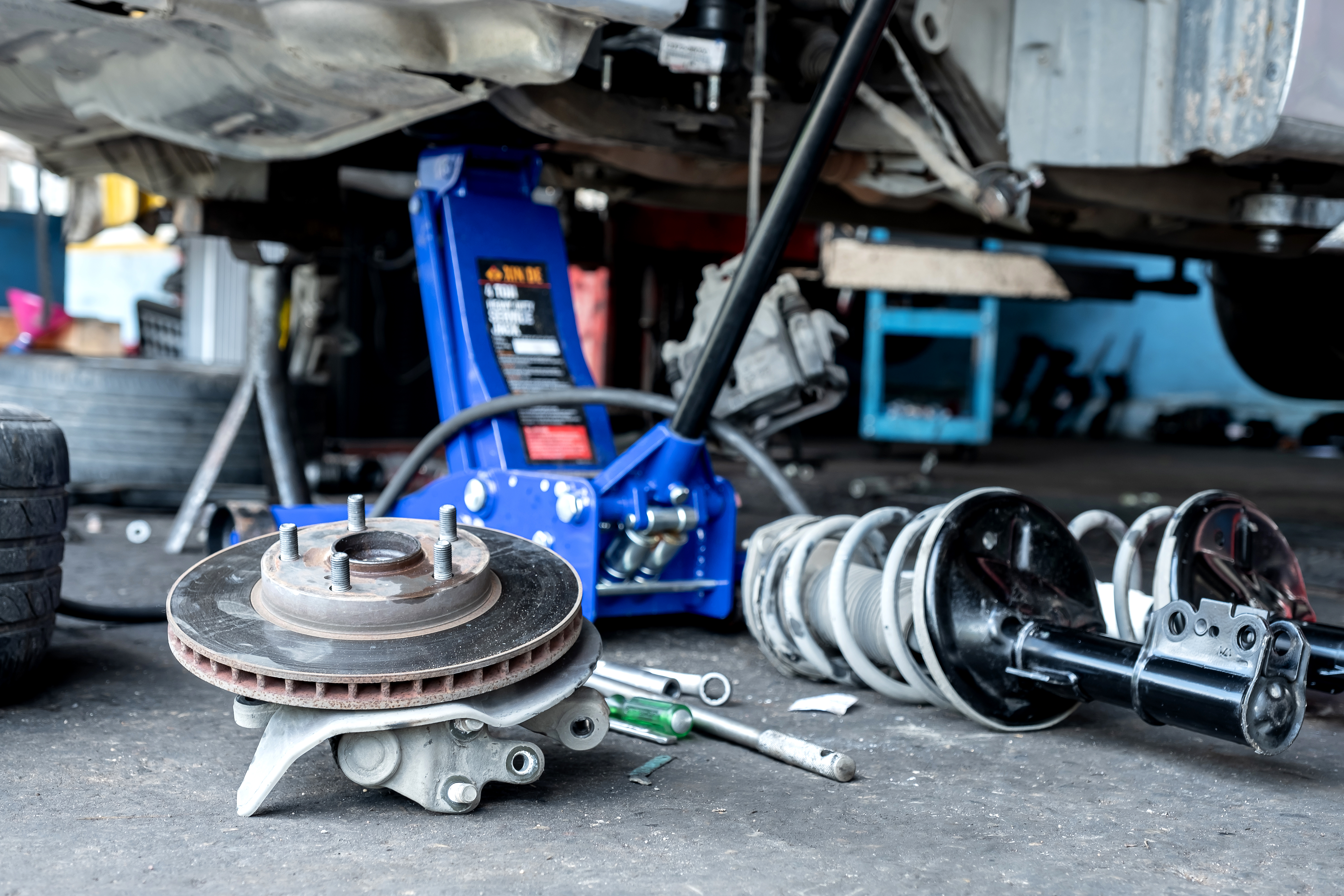 Disassembled brake rotors and calipers on workshop floor with vehicle lift and tools in background