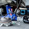 Disassembled brake rotors and calipers on workshop floor with vehicle lift and tools in background