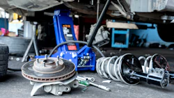 Disassembled brake rotors and calipers on workshop floor with vehicle lift and tools in background