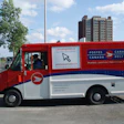 Red and white Canada Post delivery truck with postal service branding and website information on city street