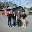 Four employees standing outside Capstan automotive service facility with red garage doors