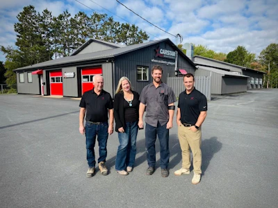 Four employees standing outside Capstan automotive service facility with red garage doors