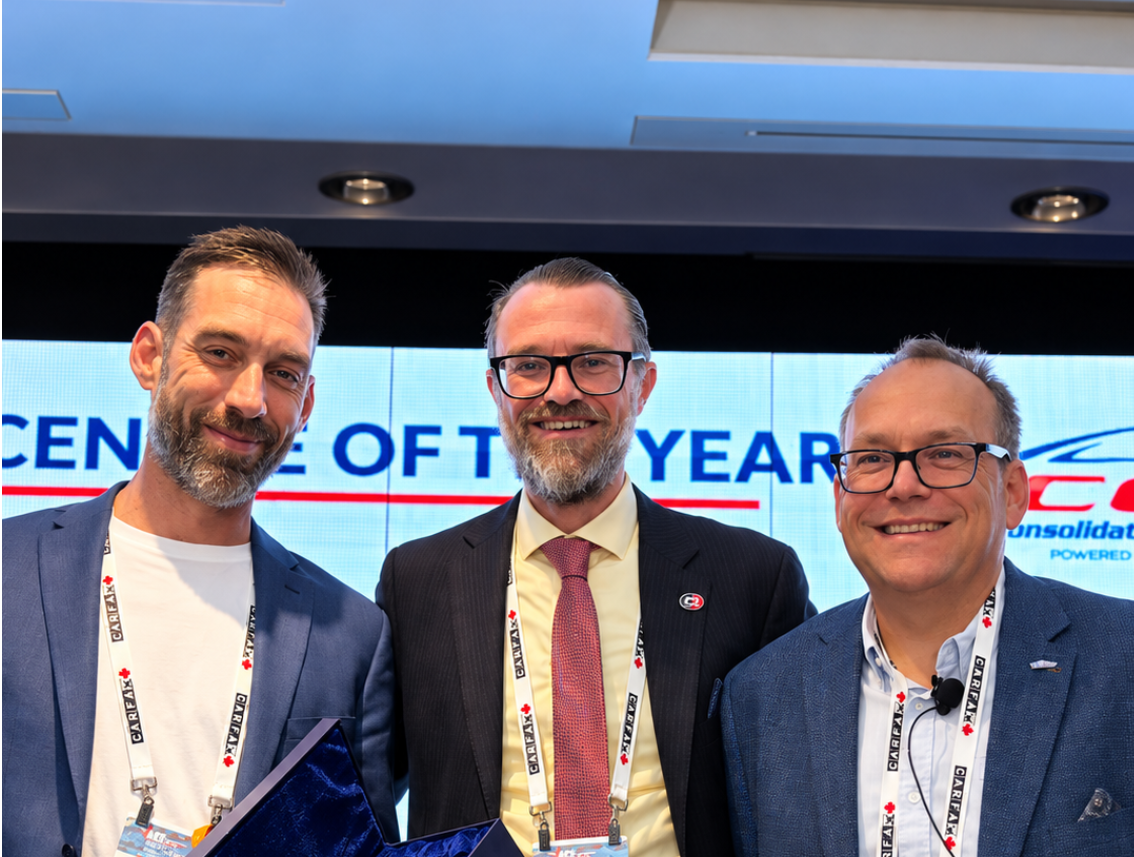 Three professionals in business attire at a corporate event with conference badges and award recognition display