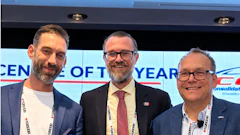 Three professionals in business attire at a corporate event with conference badges and award recognition display