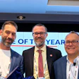 Three professionals in business attire at a corporate event with conference badges and award recognition display