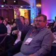 Professional attendees at a formal dinner event with purple ambient lighting and stage setup in background