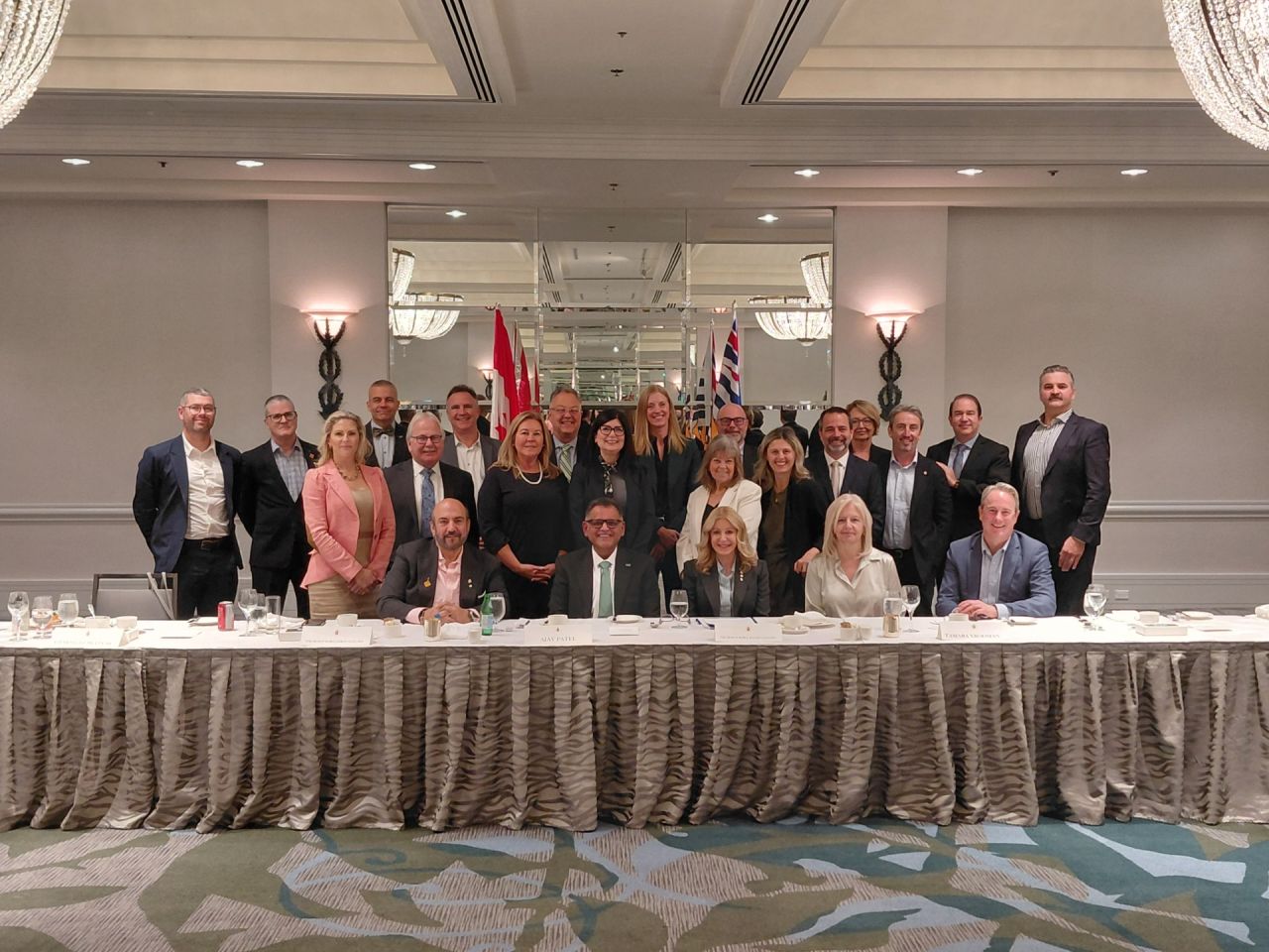 Group of business professionals posing at formal corporate event with draped table and flags