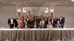 Group of business professionals posing at formal corporate event with draped table and flags