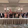 Group of business professionals posing at formal corporate event with draped table and flags