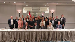 Group of business professionals posing at formal corporate event with draped table and flags