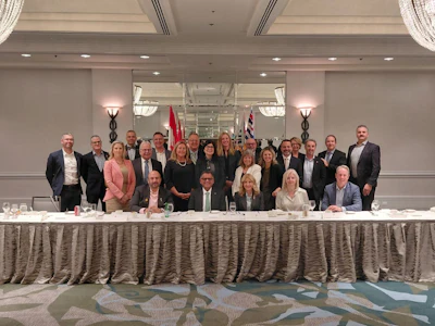 Group of business professionals posing at formal corporate event with draped table and flags