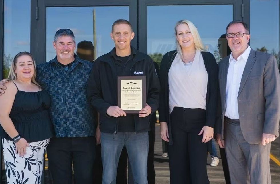 Six people pose together at a grand opening event, with one holding a certificate plaque