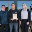 Six people pose together at a grand opening event, with one holding a certificate plaque