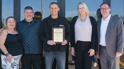 Six people pose together at a grand opening event, with one holding a certificate plaque