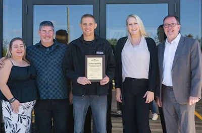 Six people pose together at a grand opening event, with one holding a certificate plaque