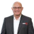 Professional headshot of a smiling man wearing glasses and gray blazer with white shirt Headshot