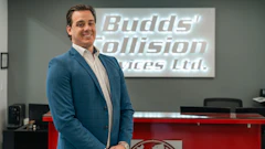 Professional man in blue blazer standing in modern office with Budds' Collision Services Ltd. signage