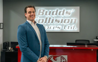 Professional man in blue blazer standing in modern office with Budds' Collision Services Ltd. signage