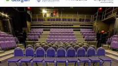Empty auditorium with purple theater seats arranged in tiered rows on a beige stage floor