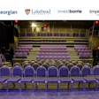 Empty auditorium with purple theater seats arranged in tiered rows on a beige stage floor