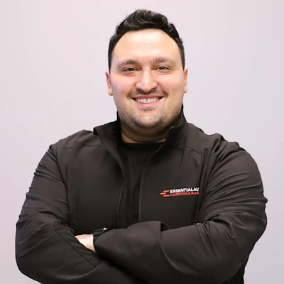 Professional headshot of smiling man in black EssentialAu branded jacket against neutral background