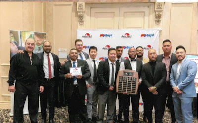 Group of businessmen in formal attire holding awards at corporate event with Assurant and Boyd sponsor logos on backdrop