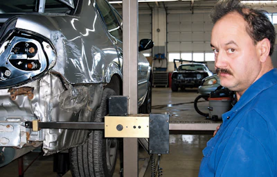Mechanic examines damaged car front end with diagnostic equipment in automotive repair shop