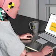 Person wearing pink crash test dummy head at desk with laptop showing test results