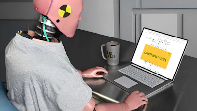 Person wearing pink crash test dummy head at desk with laptop showing test results