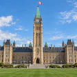 Parliament of Canada Centre Block with copper roof and clock tower under blue sky with clouds